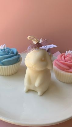 three cupcakes on a white plate with a small bunny figurine in the middle