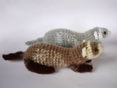 two crocheted stuffed otters sitting next to each other on a white surface