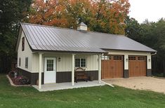 a two car garage with an attached porch and covered in metal roofing, surrounded by trees