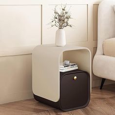 a white and black side table with a vase on it next to a beige chair