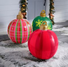 two christmas ornaments sitting on top of snow covered ground next to a door and wreath