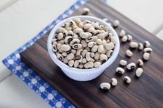 a white bowl filled with black eyed peas on top of a wooden cutting board next to a blue and white checkered cloth