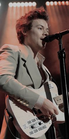 a man in a suit singing into a microphone and playing an electric guitar on stage