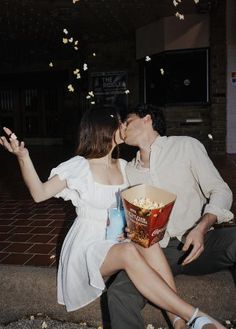 a man and woman kissing while sitting on the ground with popcorn in front of them