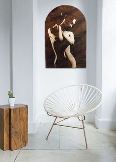 a white chair sitting in front of a painting on the wall next to a wooden table