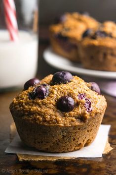 a muffin with blueberries is sitting on a napkin next to a glass of milk