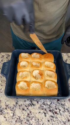 a person cutting bread with a knife on top of it in a blue pan over a granite countertop