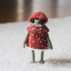 a small knitted frog wearing a red coat and white polka dot scarf on a rug