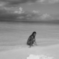 a woman kneeling down in the sand at the beach