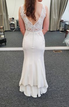 a woman in a white wedding dress looking at herself in the mirror with her back to the camera