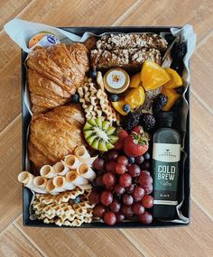 a box filled with different types of food on top of a wooden floor next to a bottle of wine