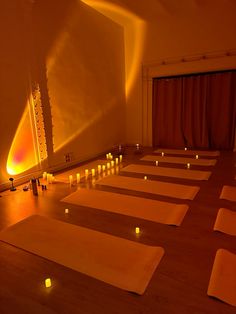 rows of yoga mats with lit candles on them in front of a large mirror and curtain