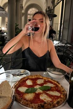 a woman sitting at a table with a pizza and glass of wine in front of her