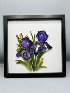 purple flowers are in a black frame on a white surface with yellow and green leaves