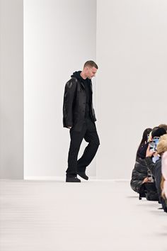 a man walking down a runway in front of a group of people wearing black clothing