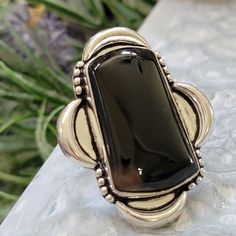 Introducing our striking Black Stone Statement Ring, a captivating piece of jewelry that combines the allure of a large, elegant black rectangular gemstone with the charm of a simple yet beautiful flower motif etched into the sterling silver ring. This statement ring features a  black gemstone and is available in a size 7.5, making it a perfect fit for those who appreciate bold and sophisticated designs. Elegant Black Gemstone: The centerpiece of this statement ring is a large rectangular black Elegant Black Jewelry With Large Stone, Black Rectangular Rings For Gifts, Black Jewelry With Rectangular Stone For Gift, Black Rectangular Ring Gift, Black Rectangular Stone Jewelry For Gift, Black Rectangular Stone Jewelry Gift, Rectangular Onyx Rings For Gifts, Rectangular Onyx Rings For Gift, Rectangular Onyx Gemstone Jewelry