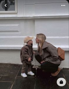 a woman kneeling down next to a little boy on the ground in front of a building