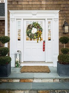 the front door is decorated with wreaths and an outdoor lantern filled with ornaments set in festive pots for guests to arrive