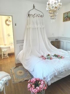 a bed with white sheets and pink flowers on top of it, next to a chandelier