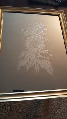 a sunflower etched in frosted glass on a table top with a gold frame