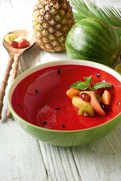 a bowl filled with fruit on top of a white wooden table next to a pineapple