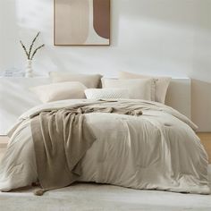 an unmade bed in a white room with beige sheets and pillows on the floor