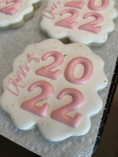 three decorated cookies with pink frosting and numbers on them are sitting on a table