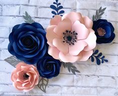 three paper flowers on a brick wall with blue and pink ones in the middle,