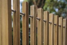 a wooden fence that is next to some trees and bushes in the background, with metal bars on each side