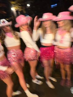 a group of women in pink hats and sequin skirts dancing on the street at night