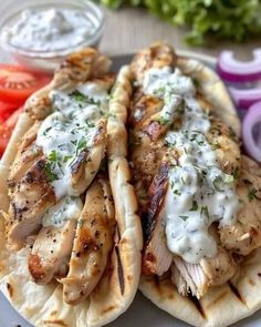 two chicken pita sandwiches on a plate with tomatoes, onions and lettuce