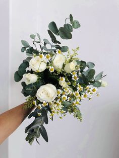 a bouquet of white roses and greenery is being held by someone's hand