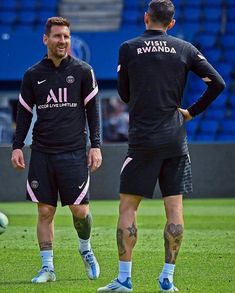 two soccer players standing on the field with their hands in their pockets and tattoos on their arms