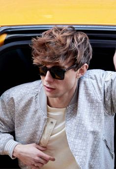 a young man in sunglasses leaning out the window of a yellow car with his hand on his head