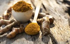 tumerical powder and ginger root on an old wooden table with two spoons