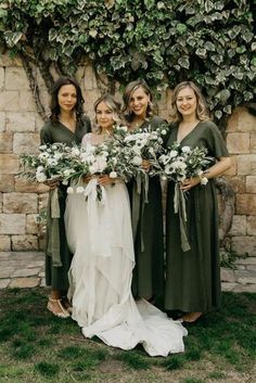 the bridesmaids are holding their bouquets in front of a stone wall with ivy growing on it