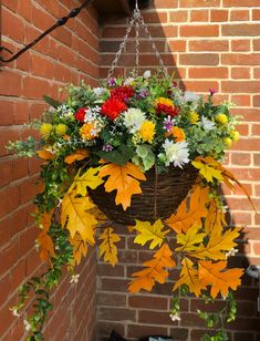 a hanging basket filled with colorful flowers and greenery next to a brick wall,