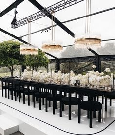 a long table with black chairs and white flowers on it is surrounded by hanging chandeliers