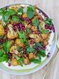 a white plate topped with cauliflower and pomegranate next to a fork