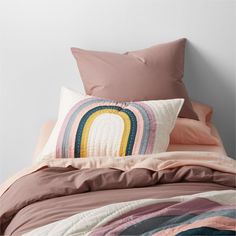 a bed with pink sheets, pillows and a rainbow pillow case on top of it