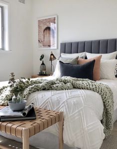 a bed with white sheets and pillows in a bedroom next to a window, coffee table