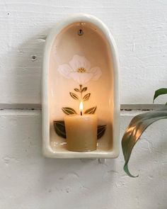 a candle is lit in a white wall mounted niche with flowers on it and leaves