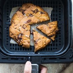 a person holding a cell phone in front of a chocolate chip cookie on a black tray