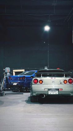 two cars parked in a garage next to each other with lights on the roof and one car being worked on