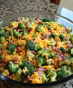 a glass bowl filled with broccoli and cheese on top of a granite counter