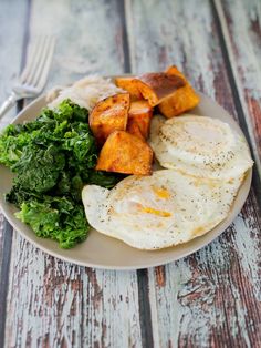 a plate with eggs, potatoes and kale on it sitting on a wooden table