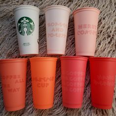 five starbucks cups with different lettering on them sitting on a carpeted surface, all lined up in the same row