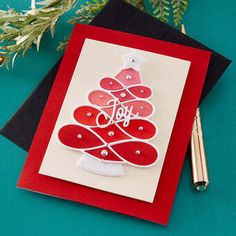 a card with a christmas tree on it next to a pen and some greenery