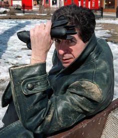 a man sitting on top of a bench wearing a leather jacket and covering his eyes