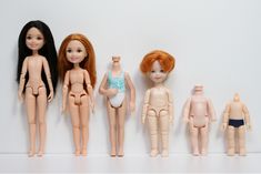 five dolls lined up next to each other on a white surface with one doll in the middle